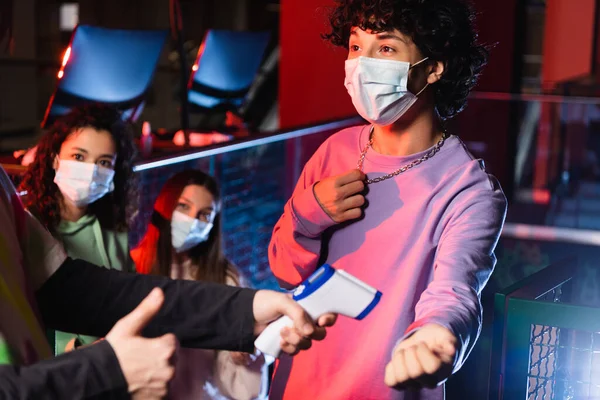 Controller of game zone showing thumb up near interracial teenagers in medical masks — Stock Photo