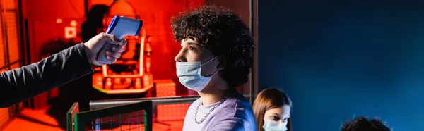 Adolescent garçon dans masque médical près contrôleur avec pyromètre et fille sur fond flou, bannière — Photo de stock