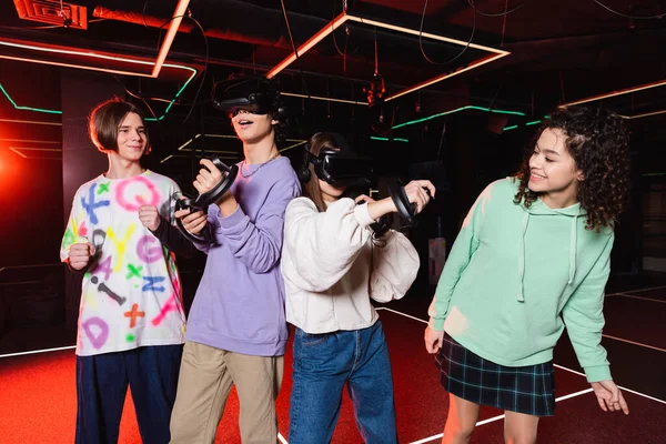 Amazed teenagers gaming in vr headsets near cheerful interracial friends — Stock Photo