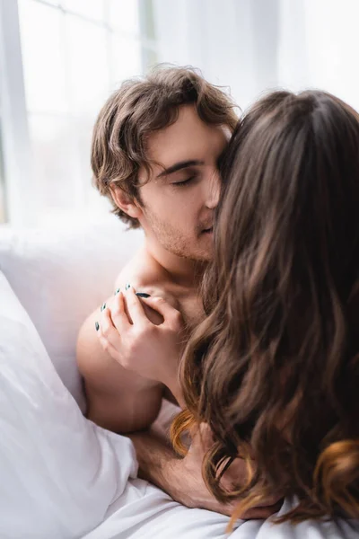 Junger Mann küsst brünette Freundin auf Bett — Stockfoto