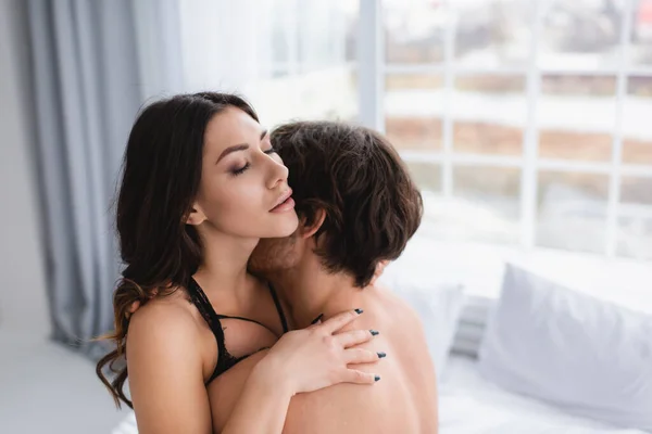 Sensual woman in bra hugging boyfriend in blurred bedroom — Stock Photo