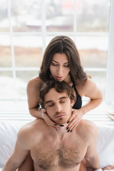 Sexy woman touching neck of muscular boyfriend in bedroom — Stock Photo