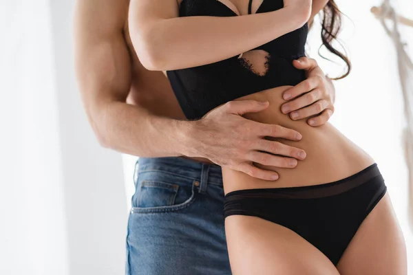 Vista recortada del hombre musculoso abrazando la cintura de la mujer sexy en lencería — Stock Photo