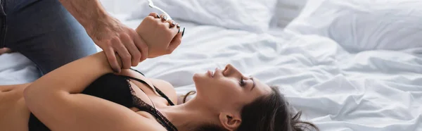 Woman in bra lying on bed near boyfriend with handcuffs, banner — Stock Photo