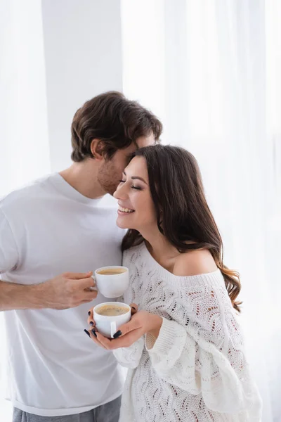 Homem beijando namorada alegre em camisola de malha com café — Fotografia de Stock