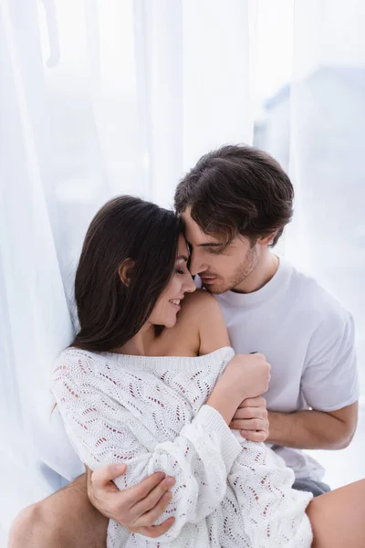 Junger Mann umarmt lächelnde Freundin im Strickpullover zu Hause — Stockfoto