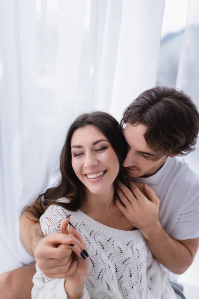 Joven abrazando y cogido de la mano de la novia alegre con los ojos cerrados - foto de stock