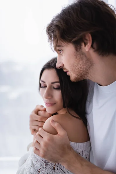 Homme embrassant petite amie brune avec les yeux fermés à la maison — Photo de stock