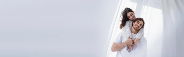 Mujer sonriendo y abrazando novio morena cerca de la ventana, pancarta - foto de stock