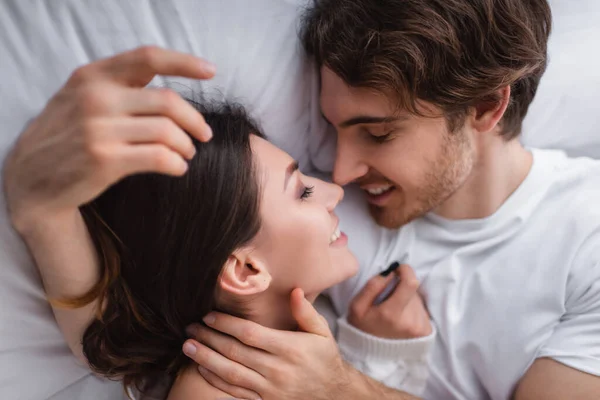 Top view of smiling couple hugging on white bedding — Stock Photo