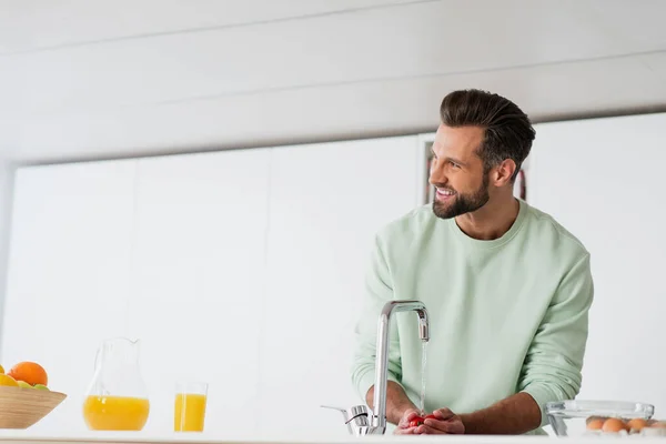 Hombre feliz lavando tomates cherry mientras se prepara el desayuno en la cocina — Stock Photo