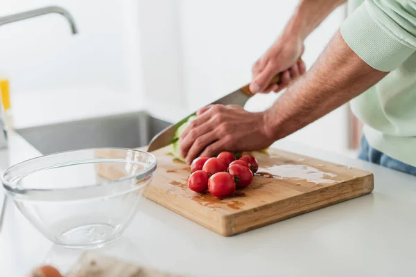 Vista recortada del hombre cortando lechuga cerca de tomates cherry en la cocina - foto de stock