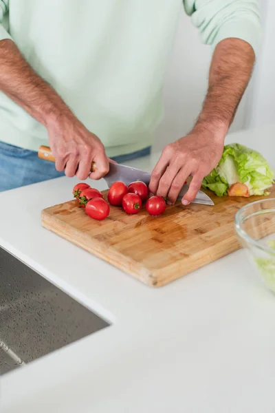 Partial view of man cutting ripe cherry tomatoes in kitchen — Stock Photo