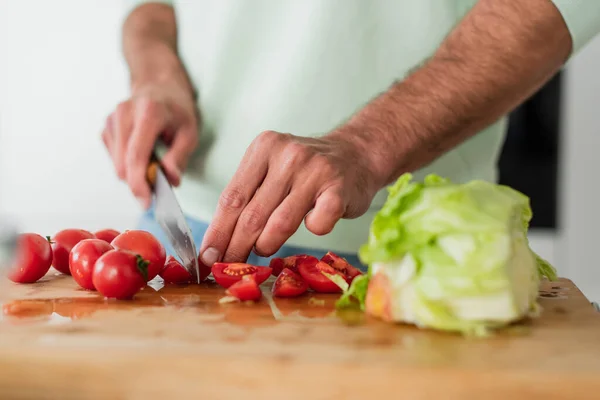 Abgeschnittene Ansicht eines Mannes, der Kirschtomaten in der Nähe von frischem Salat in der Küche schneidet — Stockfoto