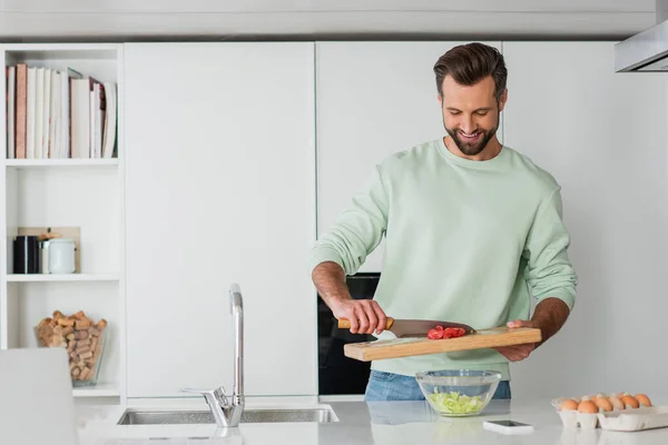 Uomo positivo sorridente mentre cucina la colazione in cucina — Foto stock