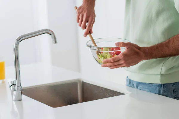 Visão parcial do homem misturando salada fresca perto de pia na cozinha — Fotografia de Stock
