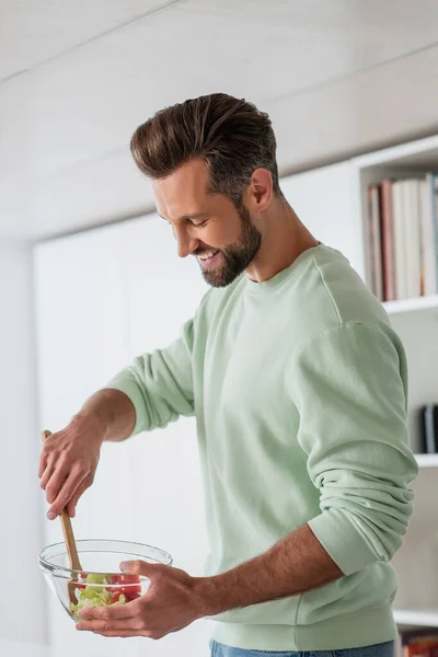 Homem feliz preparando salada de legumes para o café da manhã na cozinha — Fotografia de Stock