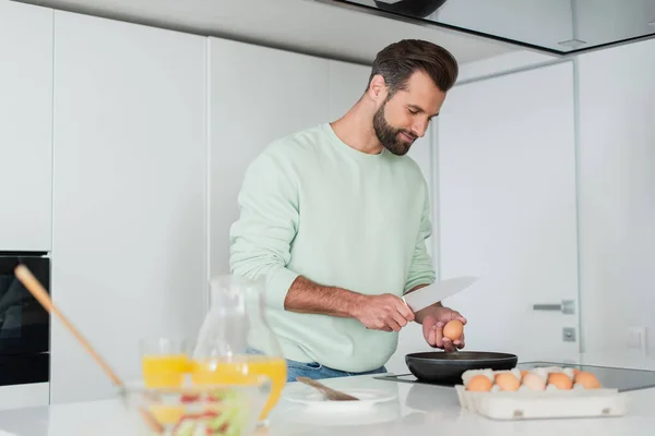 Чоловік готує сніданок з курячих яєць біля апельсинового соку на розмитому фоні — стокове фото