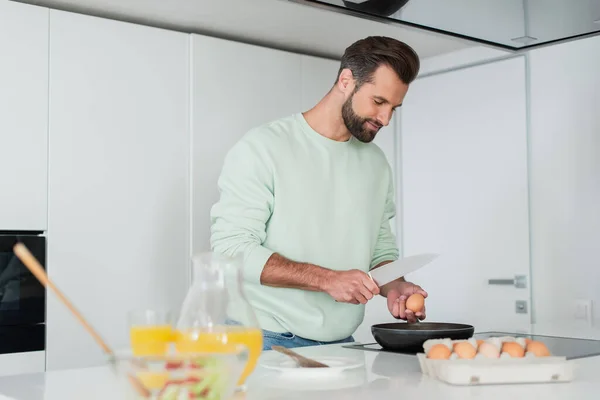 Uomo che prepara la colazione dalle uova di pollo vicino al succo d'arancia in primo piano sfocato — Foto stock