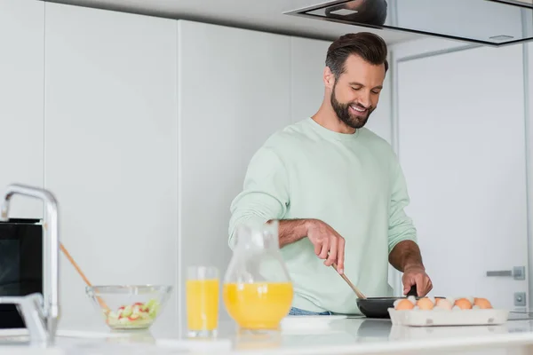 Hombre sonriente preparando el desayuno en la pluma de freír en la cocina - foto de stock