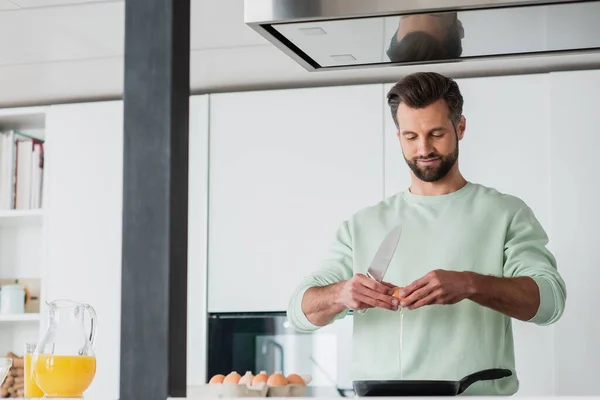 Uomo positivo frena uovo di pollo vicino alla penna per friggere mentre prepara la colazione — Foto stock