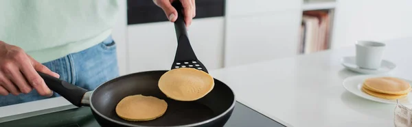 Partial view of man cooking pancakes on frying pen in kitchen, banner — Stock Photo