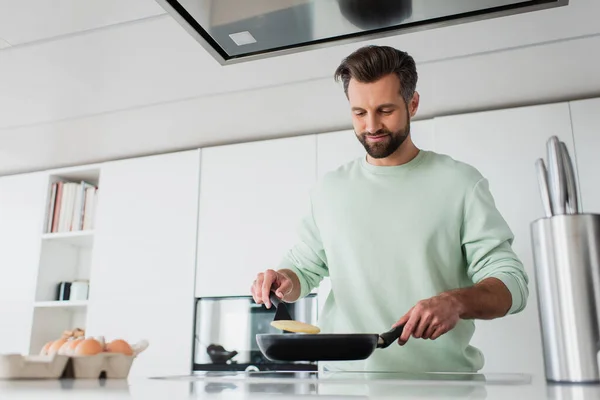 Zufriedener Mann bereitet Pfannkuchen zum Frühstück in Küche zu — Stockfoto