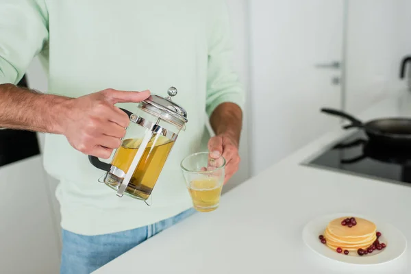 Partial view of man pouring green tea near pancakes with cranberries in kitchen — Stock Photo