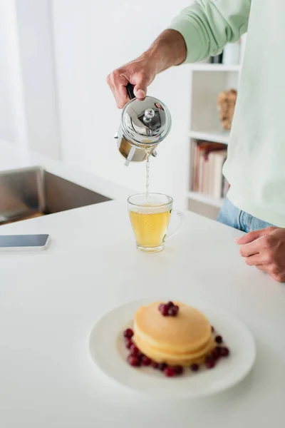 Vue recadrée de l'homme versant du thé vert près de crêpes savoureuses sur le premier plan flou — Photo de stock