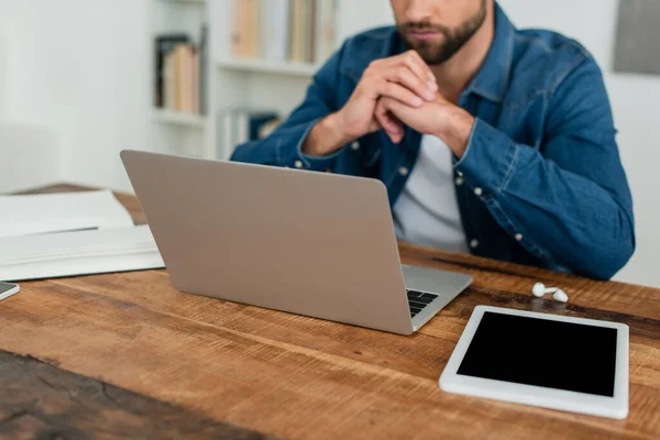 Visión parcial del teletrabajador borroso que trabaja cerca del ordenador portátil y la tableta digital con la pantalla en blanco - foto de stock