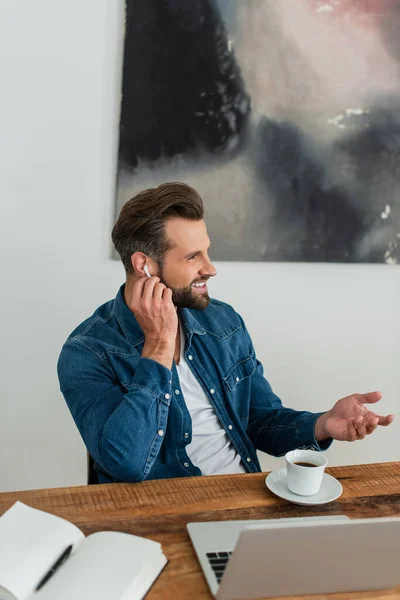 Happy freelancer adjusting earphone while sitting at workplace — Stock Photo