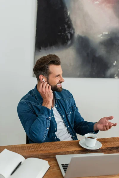 Freelancer feliz ajustando fone de ouvido enquanto sentado no local de trabalho — Fotografia de Stock