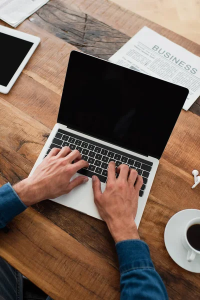 Partial view of freelancer typing on laptop near newspaper and cup of coffee — Stock Photo