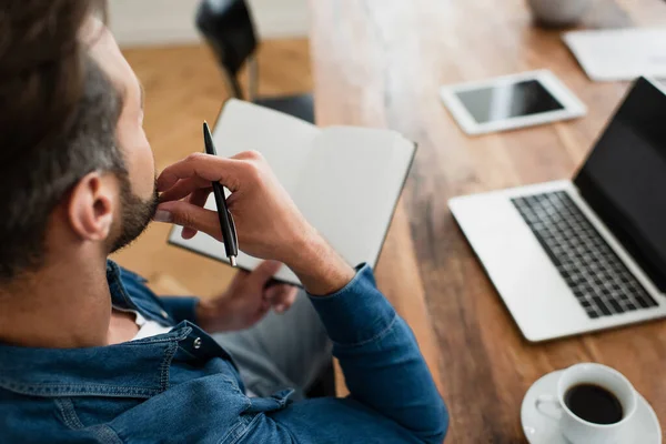 Man holding pen and notebook while working at home, blurred background — Stock Photo