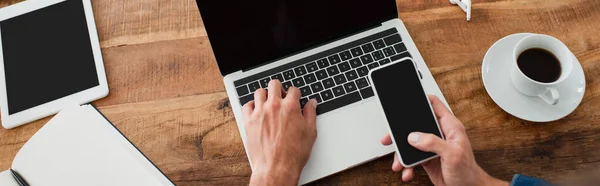 Partial view of freelancer holding smartphone with blank screen while typing on laptop, banner — Stock Photo