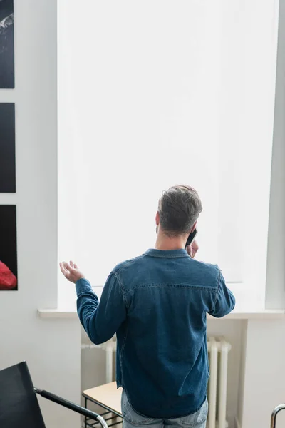 Вид ззаду людини, що розмовляє на мобільному телефоні і жестикулює біля вікна — Stock Photo