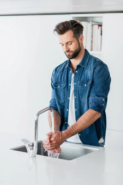 Uomo adulto in denim camicia lavaggio mani a casa — Foto stock