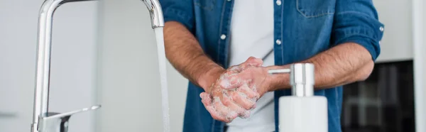 Vista recortada del hombre lavándose las manos cerca de un recipiente borroso con jabón, pancarta - foto de stock