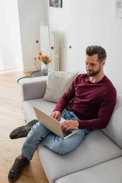 Erwachsener Mann tippt auf Laptop auf Couch im Wohnzimmer — Stockfoto