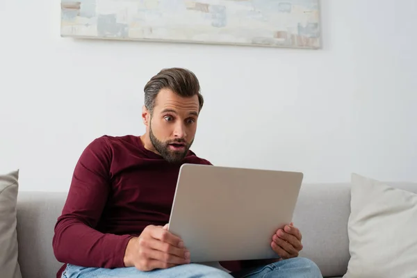 Homme surpris assis sur le canapé et regardant ordinateur portable — Photo de stock