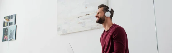 Sonriente hombre mirando hacia otro lado mientras escucha música en auriculares inalámbricos, banner - foto de stock