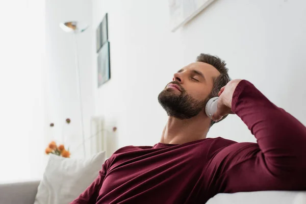 Relaxante homem ouvindo música em fones de ouvido sem fio com olhos fechados — Fotografia de Stock