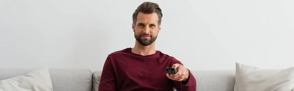 Hombre positivo haciendo clic en los canales mientras ve la televisión en casa, bandera - foto de stock