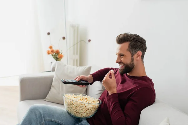 Смеющийся человек ест попкорн во время просмотра комедийного фильма в гостиной — стоковое фото