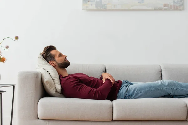 Вид сбоку человека в повседневной одежде, спящего дома на диване — стоковое фото