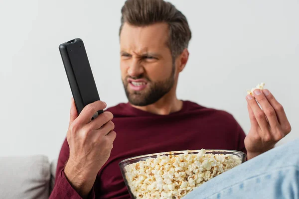 Uomo scontento con popcorn guardando telecomando tv, sfondo sfocato — Foto stock