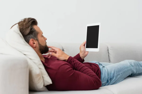 Homme adulte tenant tablette numérique tout en se reposant sur le canapé à la maison — Photo de stock