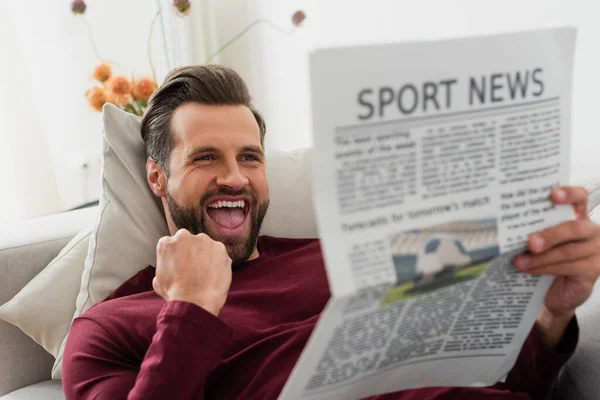 Hombre emocionado mostrando gesto de triunfo mientras lee noticias deportivas en casa - foto de stock