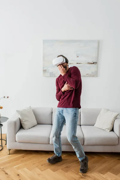 Homem assustado no fone de ouvido vr cobrindo boca com mão enquanto joga em casa — Fotografia de Stock