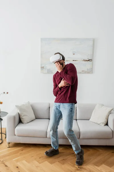 Homme effrayé dans vr casque couvrant la bouche avec la main tout en jouant à la maison — Photo de stock